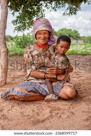 a bushmen San child from Central Kalahari, village New Xade in Botswana, held by his grandmother, in the yard of her home
