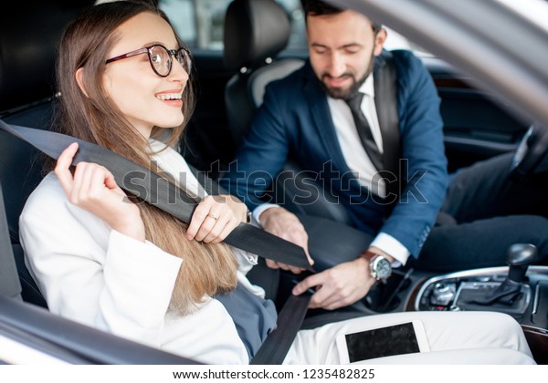 Businesman fastening belt to a woman worrying about\
her safety in the\
car