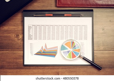 Business accessories (diary, folder with documents, pen, pencil, cactus), charts, plans, computer, mobile phone on wooden desktop