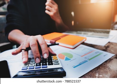 Business or accountant concept, man holding pen using calculator for calculate financial & budget & tax data document with notebook and laptop computer in working on wood desk in office. - Shutterstock ID 788521537