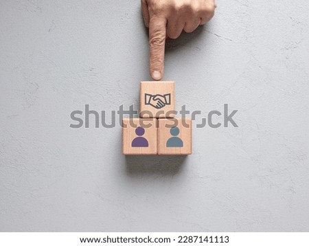 Business agreement or deal. Partnership and cooperation between parties. Mediation. Male hand puts a wooden cube with handshake agreement symbol between the cubes with person icons.
