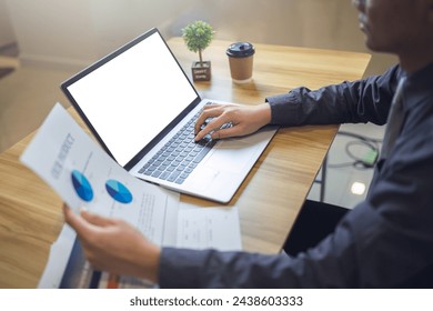 Business analyst reviewing pie charts on documents with a laptop with mockup screen on a wooden desk. - Powered by Shutterstock