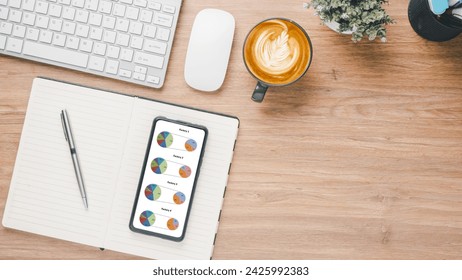 Business analytics concept, Overhead view of a business desk featuring a smartphone displaying pie charts, alongside a keyboard, notebook, coffee cup, and photography equipment.