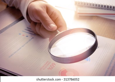 Business analytics and statistics. Businessman study report using a magnifying glass. 