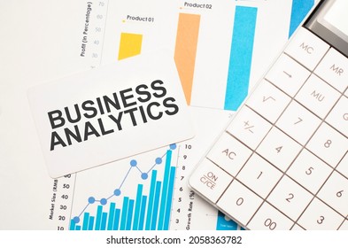 Business Analytics, Text Concept. Office Workplace Table With Calculator, Graphs, Reports And The Text Business Analytics On A Small Piece Of Paper On Multicolored Background.