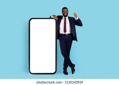 Business App. Cheerful African American Businessman Standing Near Big Blank Smartphone And Showing Thumb Up, Happy Black Male In Suit Demonstrating Copy Space For Online Advertisement, Mockup