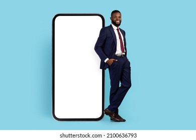 Business App. Handsome Black Male Entrepreneur In Suit Leaning At Big Blank Smartphone With White Screen, African American Businessman Demonstrating Copy Space For Application Design, Mockup - Powered by Shutterstock