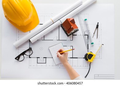 Business, Architecture, Building, Construction And People Concept - Close Up Of Architect Hand With Blueprint And Architectural Tools Writing To Notebook