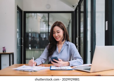 Business Asian Woman Using Smartphone For Do Math Finance On Wooden Desk In Office, Tax, Accounting, Financial Concept