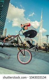 Business Bay, Dubai, United Arab Emirates - 02/12/2014: Skate Park Young Filipino Male BMX Bike Rider Performing A Flip, Stunt Or Jump With Burj Khalifa In Background With Blue Sky And Clouds