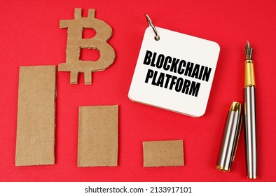 Business and bitcoin concept. On a red surface lie a bitcoin symbol, a graph, a pen and a notepad with the inscription - Blockchain platform