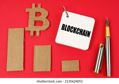 Business and bitcoin concept. On a red surface lie a bitcoin symbol, a graph, a pen and a notepad with the inscription - Blockchain