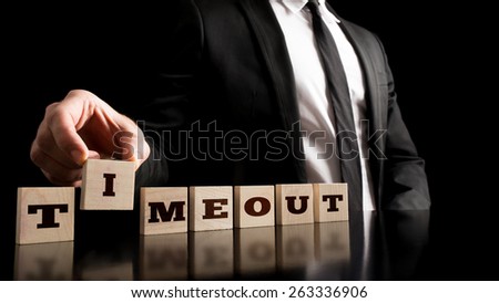 Business Break Concept - Businessman Arranging Small Wooden Blocks with word Timeout on a Pure Black Background.
