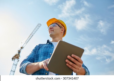 Business, Building, Industry, Technology And People Concept - Smiling Builder In Hardhat With Tablet Pc Computer Over Group Of Builders At Construction Site