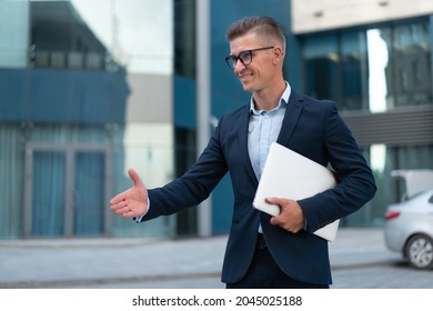 Business. Businessman Giving Hand For Handshake Welcome Gesture. Adult Caucasian Male Business Person Holding Closed Laptop Give Hand Ready Handshake Office Building Background