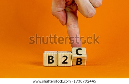 Business to Business or Busness to Consumer. Businessman turns a cube and changes words 'B2C' to 'B2B' or vice versa. Business, B2B or B2C concept. Beautiful orange background, copy space.