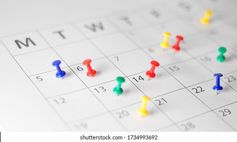 Business calendar page busy scheduling, time management, deadlines and events planning concept with many colorful push pins on a monthly paper calendar page.
