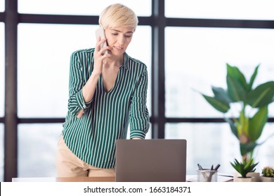 Business Calls. Entrepreneur Lady Talking On Mobile Phone Standing Near Laptop Computer In Modern Office. Selective Focus, Free Space