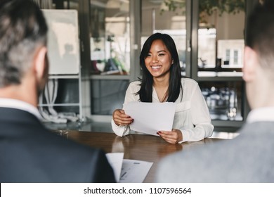 Biznes, kariera i koncepcja pośrednictwa - młoda azjatycka kobieta uśmiechająca się i trzymająca CV, siedząc przed dyrektorami podczas spotkania korporacyjnego lub rozmowy kwalifikacyjnej