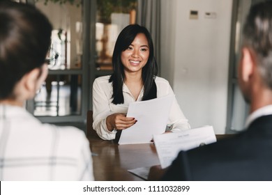 Business, career and recruitment concept - young asian woman smiling and holding resume while interviewing as candidate for job in big company
