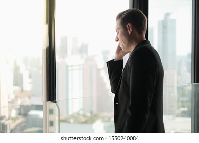 business caucasian handsome man standing in working with talking smart phone in workplace near window - Shutterstock ID 1550240084