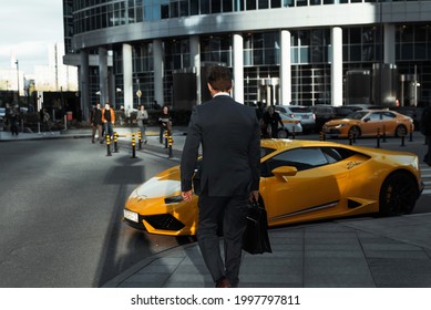 Business center of the city. Businessman in a jacket and with a briefcase walking down the street near a yellow Lamborghini, rear view. Success, wealth concept. Russia, Moscow 13.05.2021