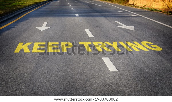 Business challenge with effort concept and\
success idea Keep trying word with white dividing lines and arrow\
on black asphalt road\
surface.