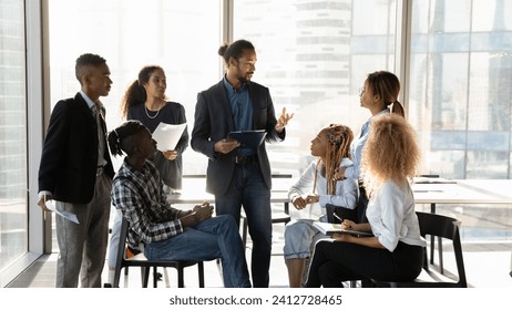 Business coaching. Young black male experienced mentor speak to mixed race group of students interns at seminar workshop. Interested millennial staff engaged in practical training on sales management - Powered by Shutterstock