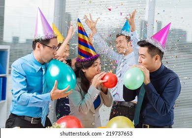 Business colleagues blowing up balloons at the office party