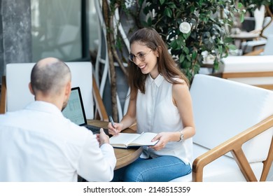 Business Colleagues Discussing Documents At A Table In An Internet Cafe.