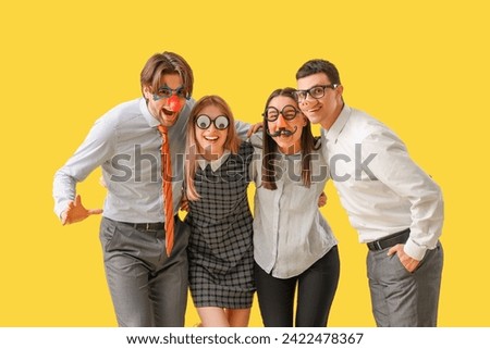 Business colleagues in funny disguise hugging on yellow background. April Fools' Day celebration