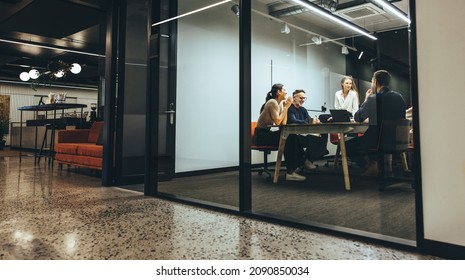 Business colleagues having a meeting in a transparent boardroom. Group of happy business professionals having a discussion during a briefing. Diverse businesspeople collaborating on a new project.