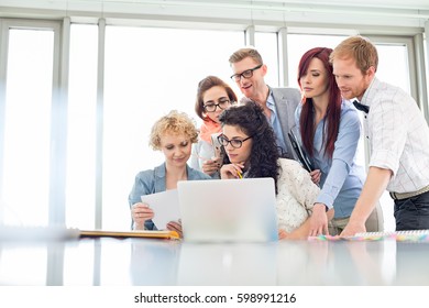 Business colleagues with laptop analyzing document in creative office