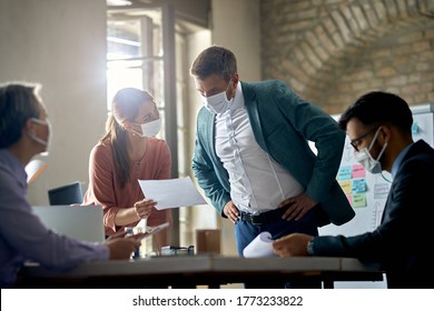 Business colleagues with protective face masks analyzing reports on a meeting in the office. - Powered by Shutterstock