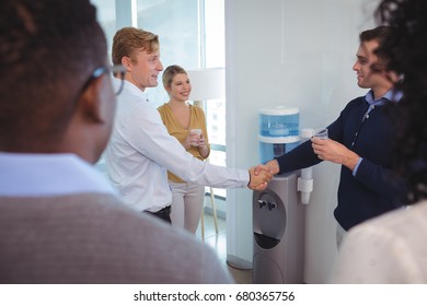Business colleagues shaking hands while holding drinking glass at office - Shutterstock ID 680365756