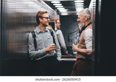 Business colleagues smiling and chatting in elevator during casual moment, holding drinks and backpacks, creating relaxed yet professional mood
