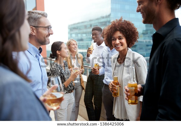 Business colleagues talking and drinking\
together on a balcony in the city after\
work