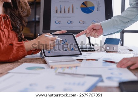 Business colleagues using tablet and computer analyzing charts, graphs, and data for real estate investment planning and financial strategy development in office environment