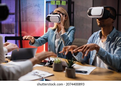 Business colleagues in VR glasses sitting at office room and gesturing with hands. Team of company workers having briefing with modern technology. Concept of people and augmented reality. - Powered by Shutterstock