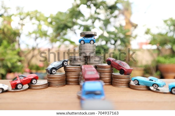 Business\
competition and winner concept, Blue toy car carry coins on top of\
ladder stair step of coin money, miniature cars drive in line level\
of money on wood table in bokeh bright\
light