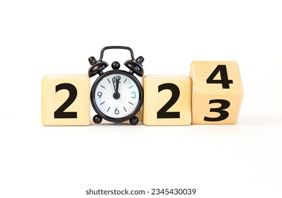 Business concept of 2024 new year symbol. Businessman turns a wooden cube and changes number 2023 to 2024. Black alarm clock. Beautiful white background, copy space. 2024 happy new year concept.