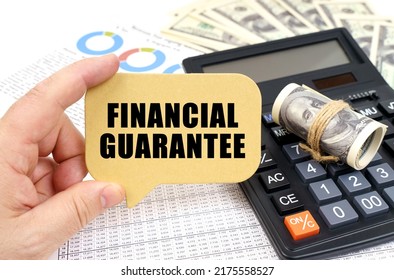 Business Concept. Against The Background Of A Calculator, Documents And Money, A Man Holds A Sign With The Inscription - Financial Guarantee