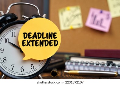 Business concept. The alarm clocks have a sticker with the inscription - DEADLINE EXTENDED. There are office items in the background in a blurry background.