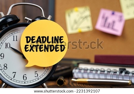 Business concept. The alarm clocks have a sticker with the inscription - DEADLINE EXTENDED. There are office items in the background in a blurry background.