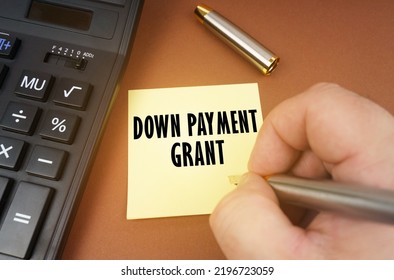 Business concept. A calculator lies on a brown surface, a hand with a pen makes an inscription on a sticker - Down Payment Grant - Shutterstock ID 2196723059