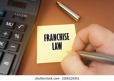 Business Concept. A Calculator Lies On A Brown Surface, A Hand With A Pen Makes An Inscription On A Sticker - Franchise Law