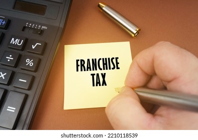 Business Concept. A Calculator Lies On A Brown Surface, A Hand With A Pen Makes An Inscription On A Sticker - Franchise Tax