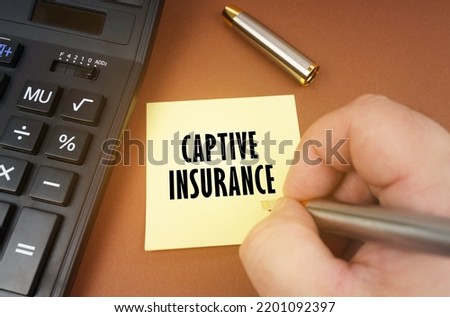 Business concept. A calculator lies on a brown surface, a hand with a pen makes an inscription on a sticker - Captive Insurance