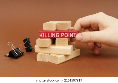 Business concept. Clamps and wooden blocks lie on a brown surface, a person takes out a red block with the inscription - KILLING POINT