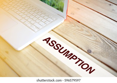 Business Concept. Computer On Wooden Table Writing ASSUMPTION